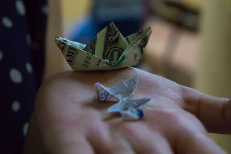 three paper boats, and a boat made with a dollar bill, on one handの写真素材