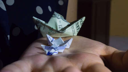 three paper boats, and a boat made with a dollar bill, on one handの写真素材