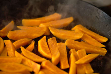 Sweet potato (yam) slices frying in a steaming pan with low oil quantity.