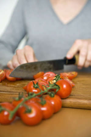 Cropped view image of the hands of a woman using a large kitchen knife to slice fresh tomatoes while preparing dinnerの写真素材