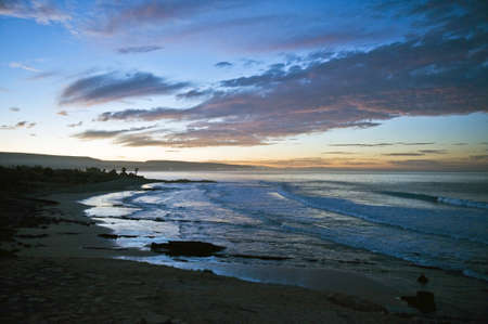 View along the coastline and ocean at sunset with an orange glow and clouds in a twilight skyの写真素材