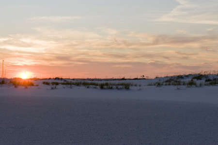 Sunset over a tropical beach with the glowing orb of the sun casting a pink light on the clouds as it sinks below the horizonの写真素材