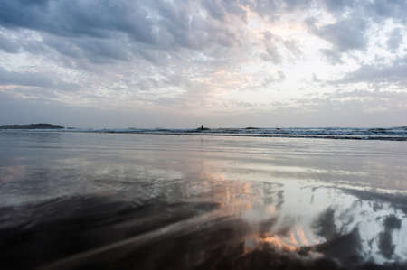 Beautiful pinky yellow reflections on the sea as the setting sun breaks through a gap in the cloudsの写真素材