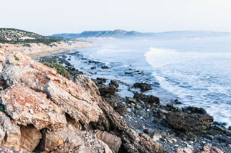 View along a scenic rocky tidal coastline and ocean with breaking waves to a distant beach with dunesの写真素材
