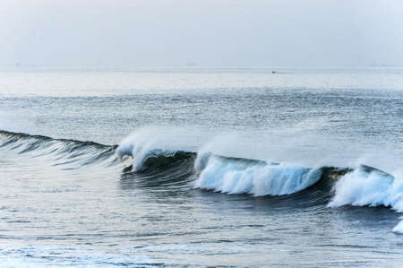 Breaking waves rolling across the ocean with flying sea spray as the wind whips the water from the crestの写真素材