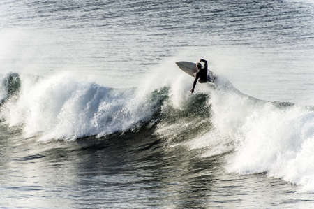 Surfer riding the crest of a big wave with his surfboard high in the air above the spray as he fights to maintain his balanceの写真素材