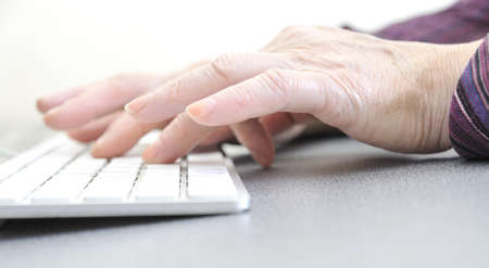 Hands of an old female typing on the keyboard, isolated on white, close-up.