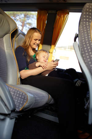 Young mother is playing games on the phone with her son, while travelling by bus 