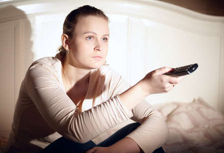 Young woman is watching tv with remote control  
