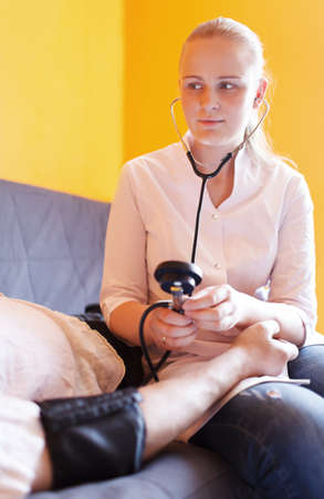 Nurse measures the patient blood pressure at home and looks with a smile
