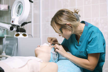 Young female beautician in a skin clinic with a patient preparing her for laser treatment fitting...