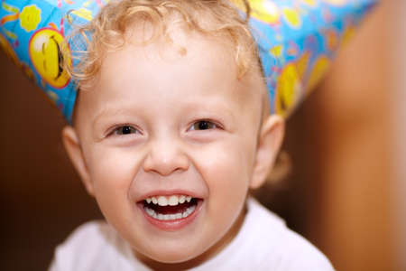 Closeup facial portrait of a happy laughing little boy with wavy blond hair looking directly into...