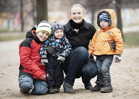 Happy attractive mother with her three young children posing outdoors together in their thick warm...