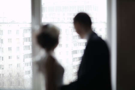 Bride and groom out of focus looking out the window. Washed out silhouettes. Romantic momentsの写真素材