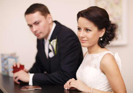 Elegant young couple standing at a reception desk with their passports with the beautiful woman smiling as she waits for serviceの写真素材