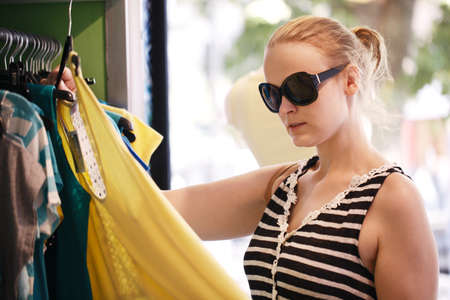 Young woman in sunglasses choosing summer clothes hanging on the racks in the shop.