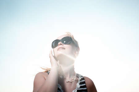 Smiling young woman in sunglasses talking on the phone and sun shines behind her back