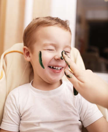 Little boy laughing as his mother paints his face streaking his cheek and dabbing his nose with black face paintの写真素材