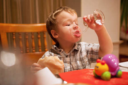 Young boy enjoying lunch draining the last drops of liquid from a glass as he holds a pie in his other handの写真素材