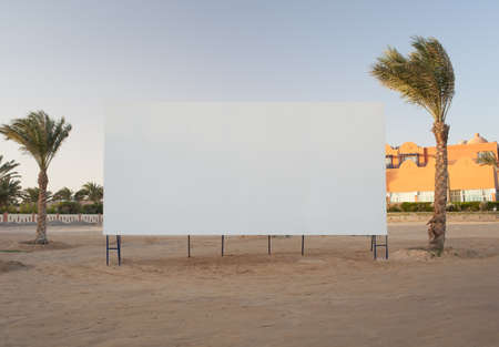 Blank white billboard with copyspace for your advertisement or movie flanked by two palm trees