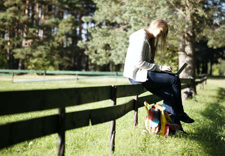 Young woman sitting on a rustic fence using her laptop computer as she enjoys the tranquillity of natureの写真素材