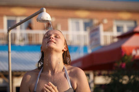 Beautiful young woman rinsing of at the beach under a fresh water shower rinsing the salt and sand...