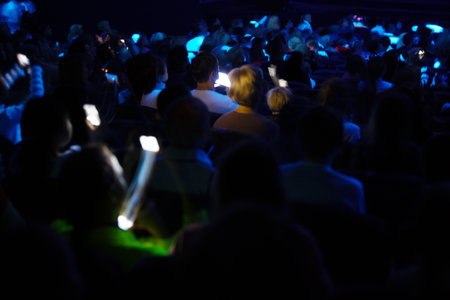 People in the audience in a darkened auditorium recording a show or special occasion with their...