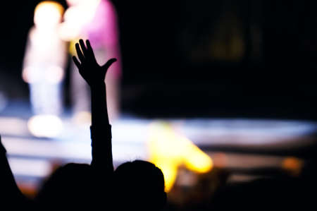 Supporter in the audience raising a hand at a live performance silhouetted against the blurred outline of people on stageの写真素材
