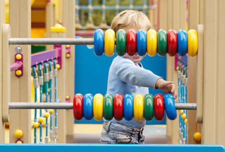 Little boy playing with an abacus with colourful rings on two bars in a childs playground as he...