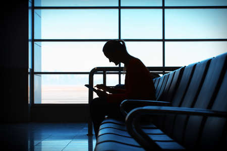 Woman in the aiport lounge sitting in chair by the window and using a tablet computer for checking...