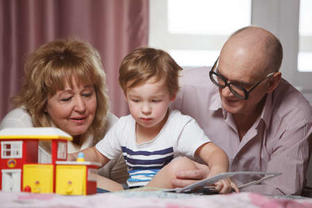 Happy grandparents spending time with their cute grandson playing with puzzle book