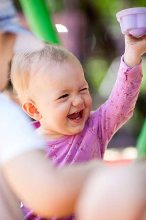 Adorable happy laughing little baby playing with a toy as it sits on its mothers lap, candid portrait over the mothers shoulderの写真素材
