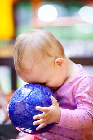 Cute little baby playing with a big blue ball sitting with its face pressed up against the ball, side viewの写真素材