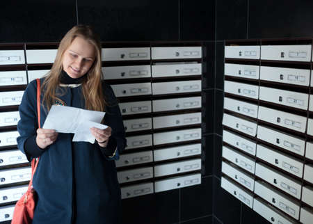 Happy woman reading received letter standing among mailboxesの写真素材