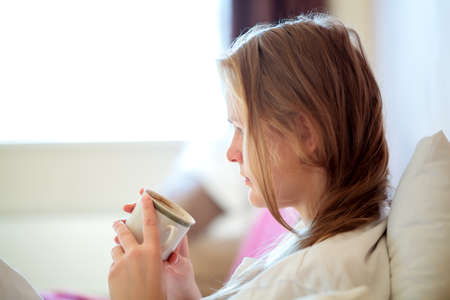 Candid side view portrait of a young blond woman drinking coffee sitting looking down at the mug in...
