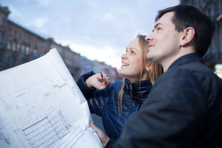 Couple standing in the street holding blueprints admiring buildingの写真素材