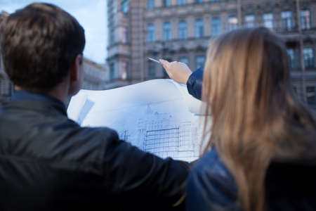 Man and woman holding blueprint while pointing and looking at a buildingの写真素材
