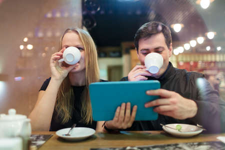 Man and woman drinking coffee while holding a smart tabletの写真素材