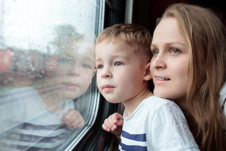 Mother and son looking through a train window as they enjoy a days travel with the small boys face...