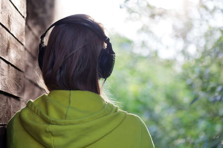 Back view of a girl in headphones listening to music outdoor  She standing by the wooden wall and enjoying nature sceneの写真素材