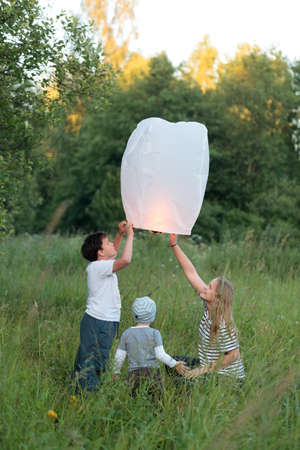Young mother and her two sons flying paper lantern outdoor in the evening  Family time spendingの写真素材