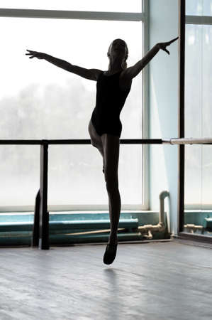 Silhouette of a ballerina making arabesque in the air  Shot against the window with sunlightの写真素材