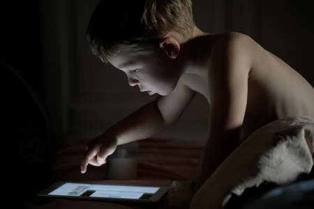 Little boy using touchpad on the bed at night  Bright pad screen lighting a childの写真素材