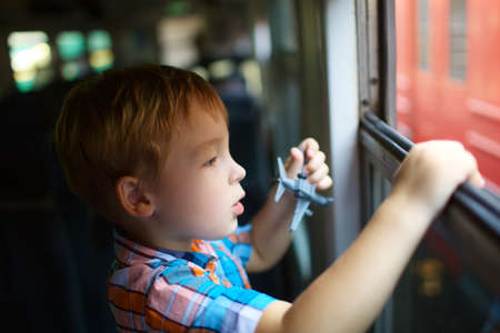 Curious little boy with toy plane looking out of open train windowの写真素材