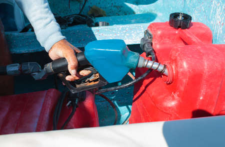 Close-up shot of a man fueling red plastic tank of a motor boat with petrolの写真素材