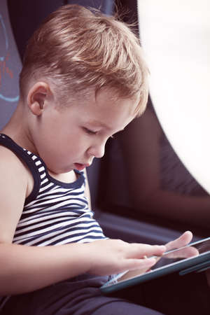 Little boy sitting by the window in the bus and using touch pad to entertain himself during the tripの写真素材