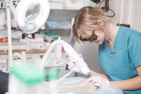 Female cosmetician in safety glasses at work. She providing a foot treatment with a laserの写真素材