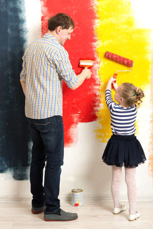 Father and little daughter having fun while painting wall in different colors. Make your life brighterの写真素材