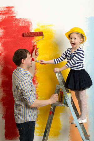 Girl and father fooling while painting wall in bright colors. Girl in hard hat standing on stepladder painting dadys noseの写真素材