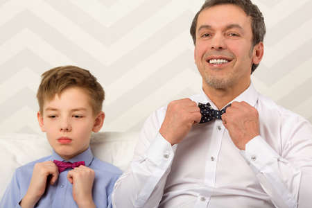 Happy dad and his serious son adjusting bowties. Preparation before celebrationの写真素材